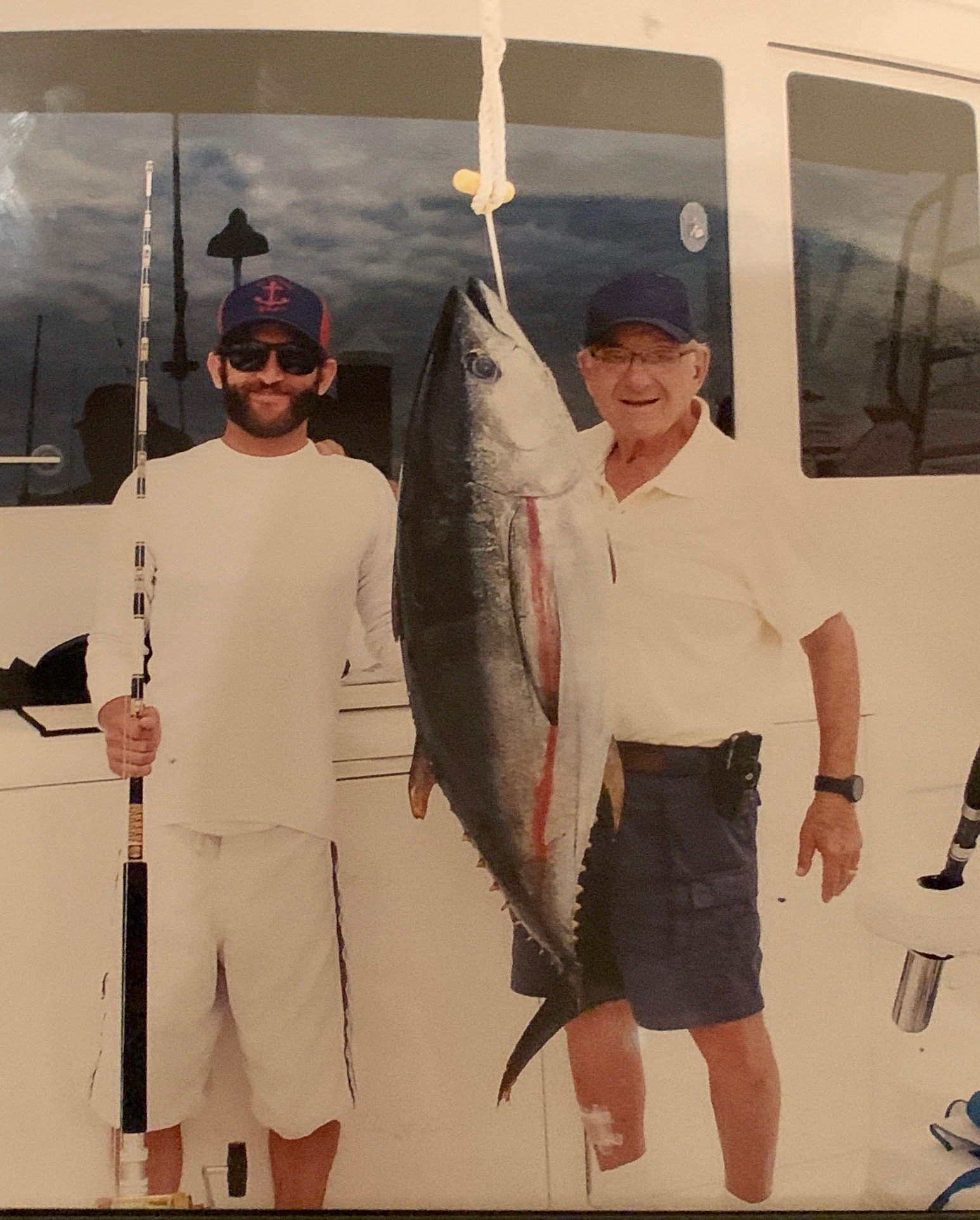 Grandfather and grandson on a boat holding a large fish they caught.
