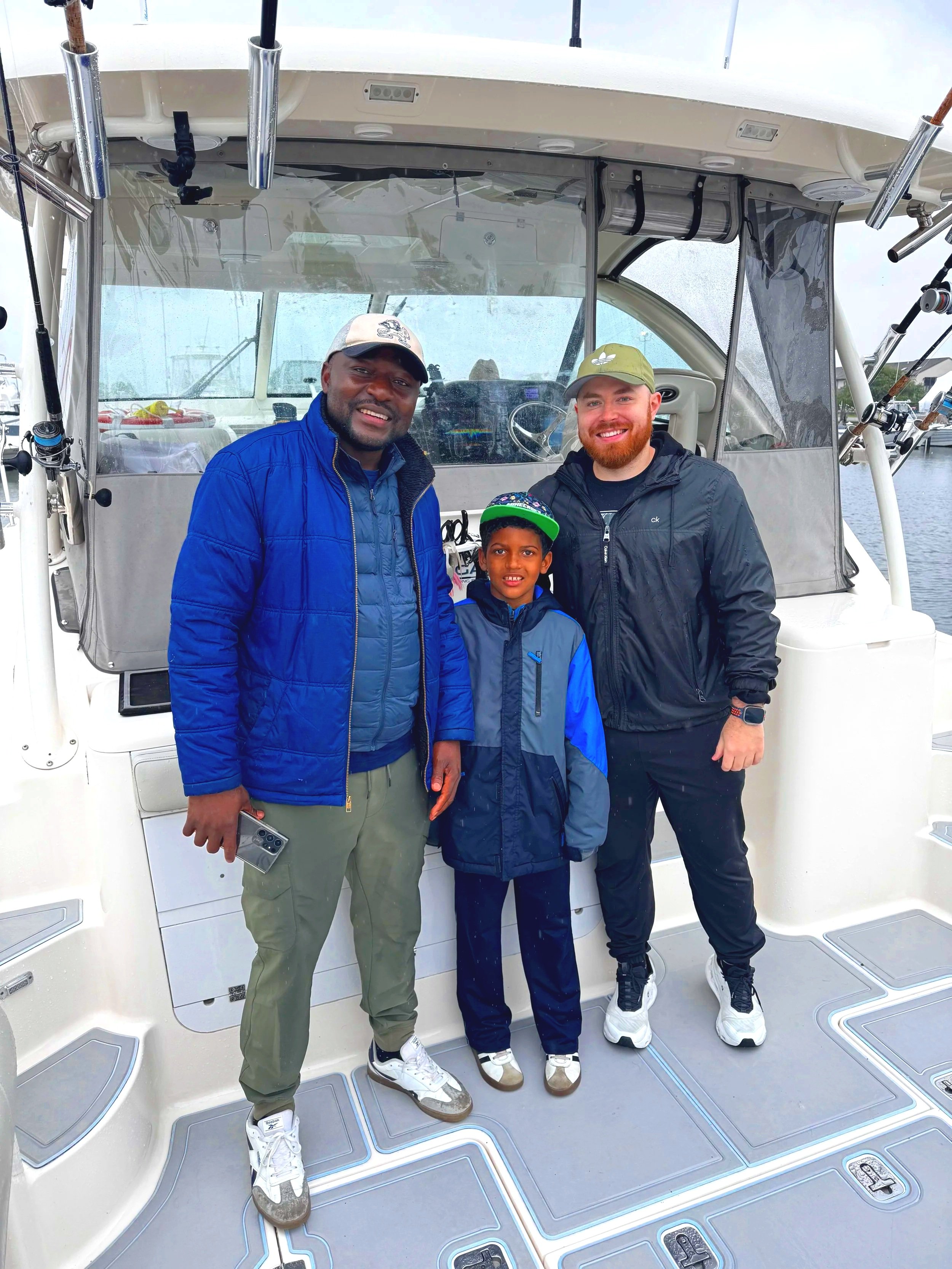 A father, son, and friend aboard a docked Legasea. They are smiling and wearing baseball hats.