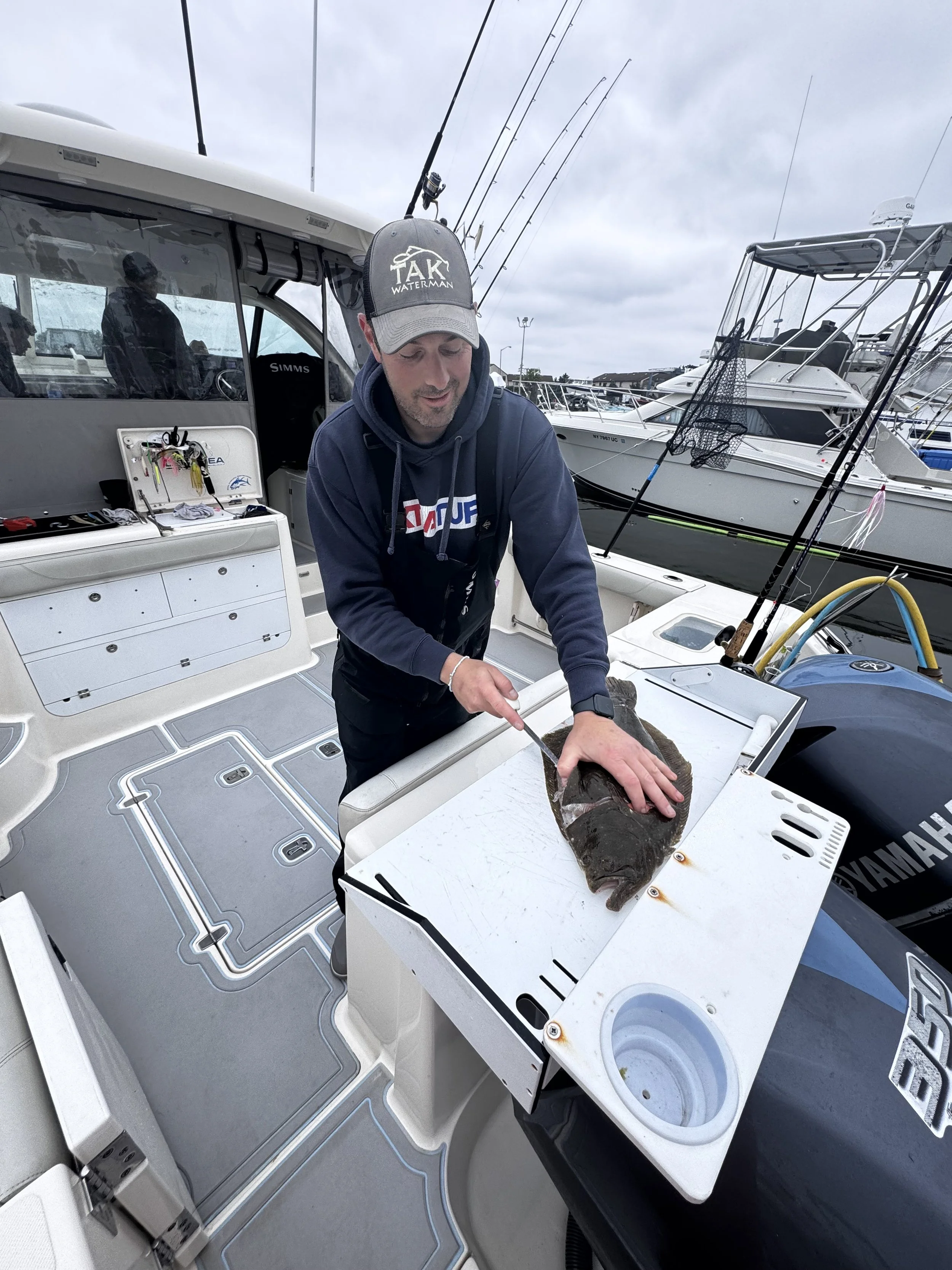 Man cleaning fish on boat docked at marina with other boats in the background.