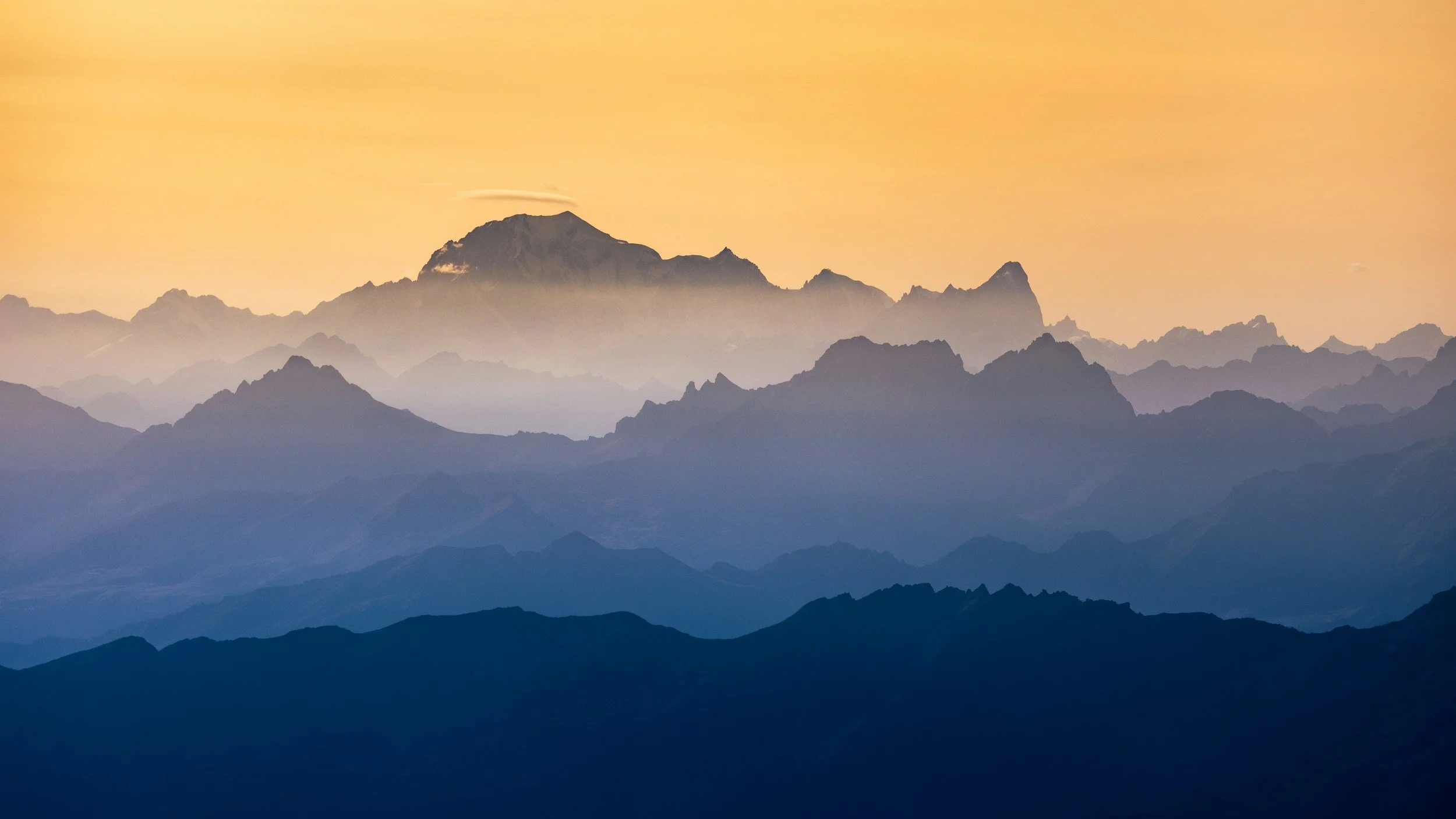 Silhouetted mountain range during sunset with layers of blue and orange hues.