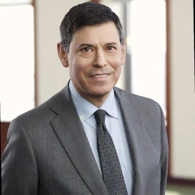 A professional man in a suit posing in an office setting with windows in the background.