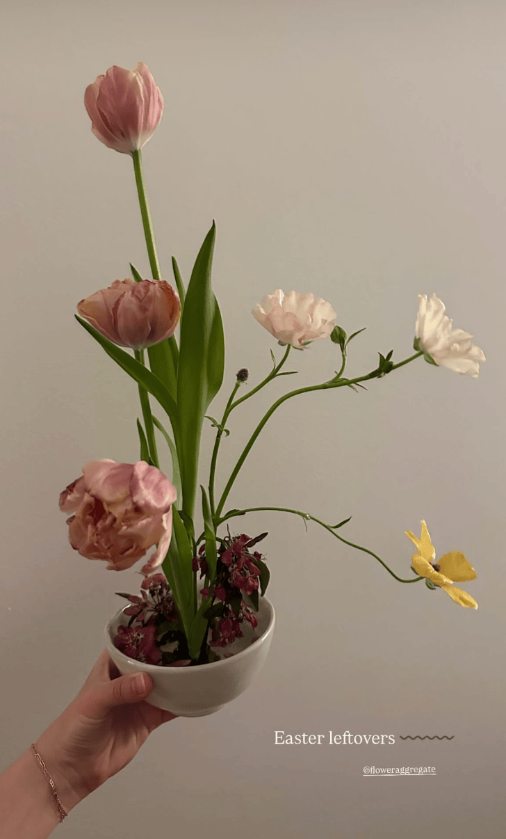 A hand holding a white bowl with wilted pink and white Easter flowers and a yellow butterfly.
