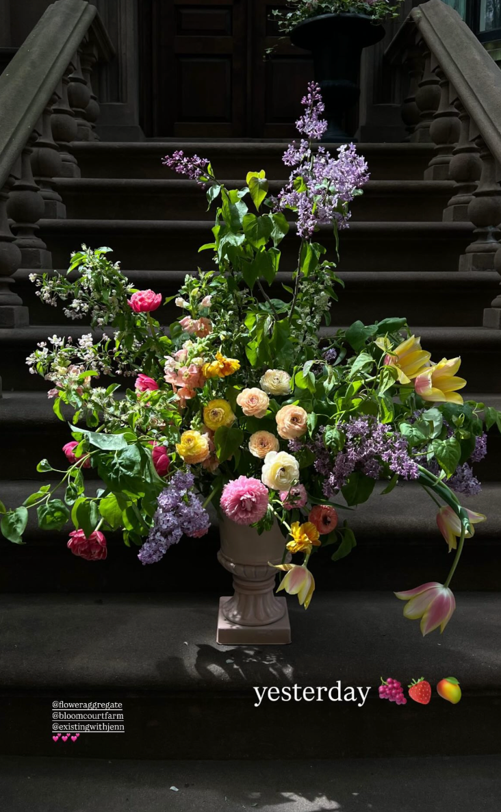 A colorful flower arrangement featuring various blooms such as pink, yellow, and white roses, lilacs, tulips, and other flowers in a white pedestal vase on a dark stone staircase."Yesterday" is written on the image with emojis of berries, strawberrie