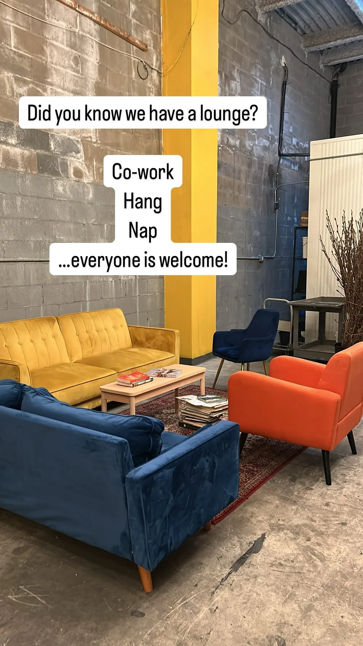 Colorful lounge area with yellow, blue, and orange sofas, a coffee table with magazines, and a stack of newspapers. There are motivational messages in speech bubbles about the lounge, promoting co-work, hang out, nap, and welcoming everyone.