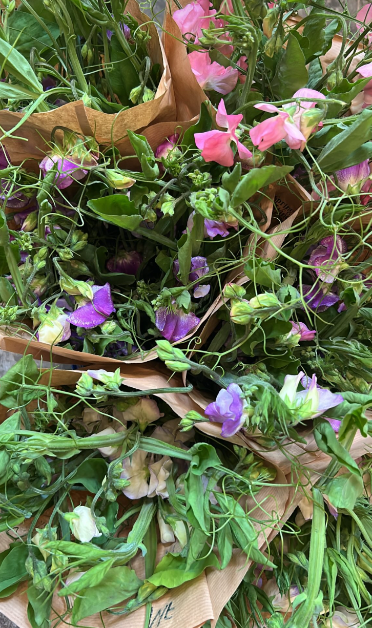 A variety of colorful flowers, including pink, purple, and white, wrapped in brown paper.