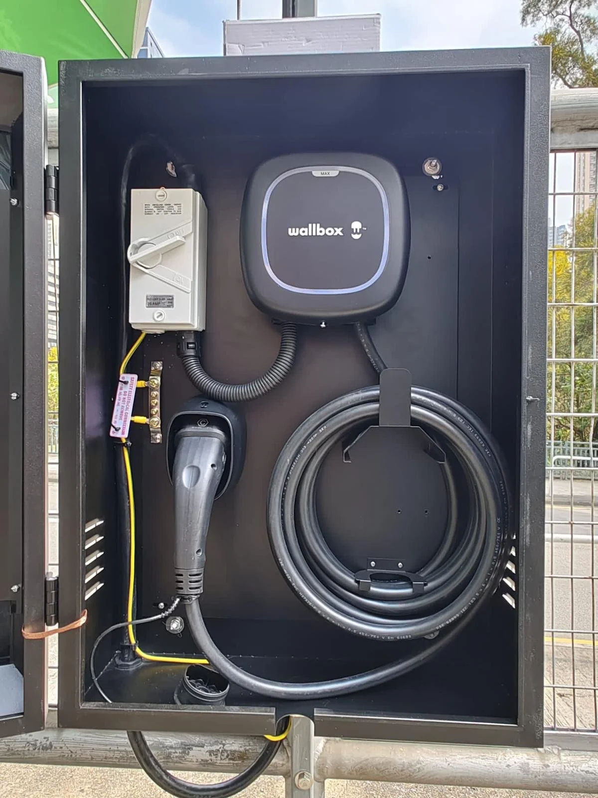 Wall-mounted electric vehicle charging station with cable and plug inside a black enclosure.