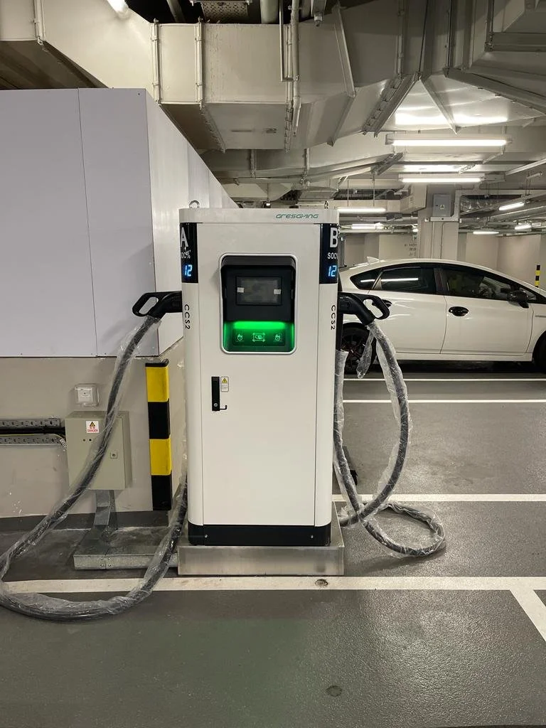 Electric vehicle charging station in a parking garage with white car nearby.