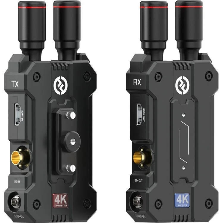 Two black wireless video transmitter and receiver units with gold-plated connectors, labeled TX and RX, featuring HDMI inputs and outputs, and built-in antennas at the top.