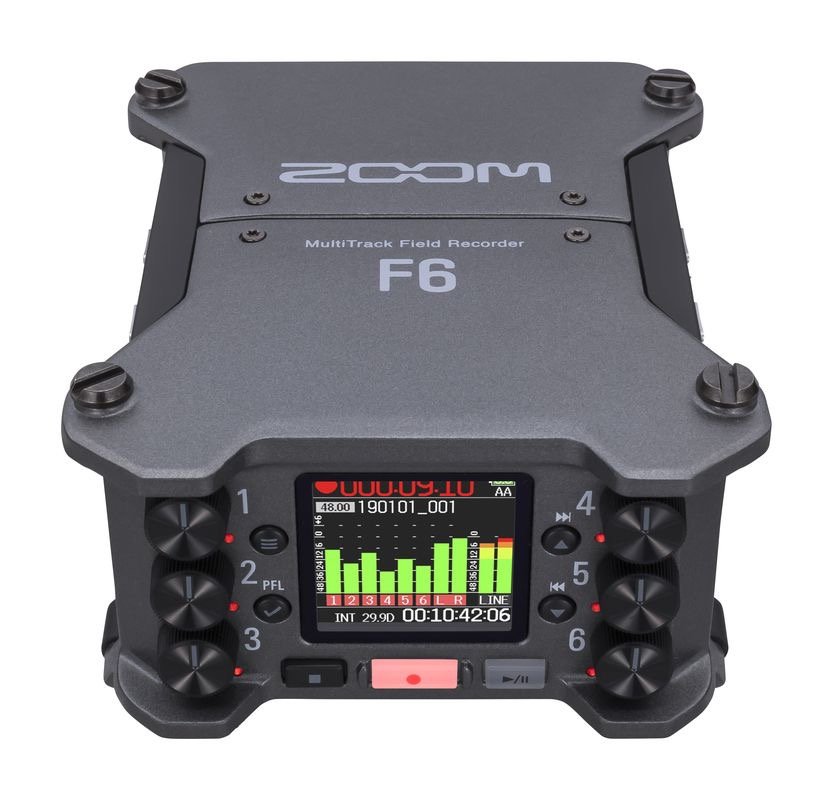 A Zoom F6 multi-track field recorder with a small color screen displaying sound levels, audio tracks, and recording time, along with various knobs and buttons.