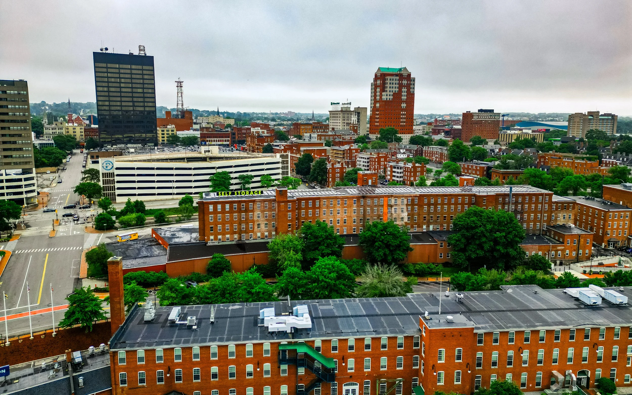 Cityscape with various buildings, trees, and overcast sky.
