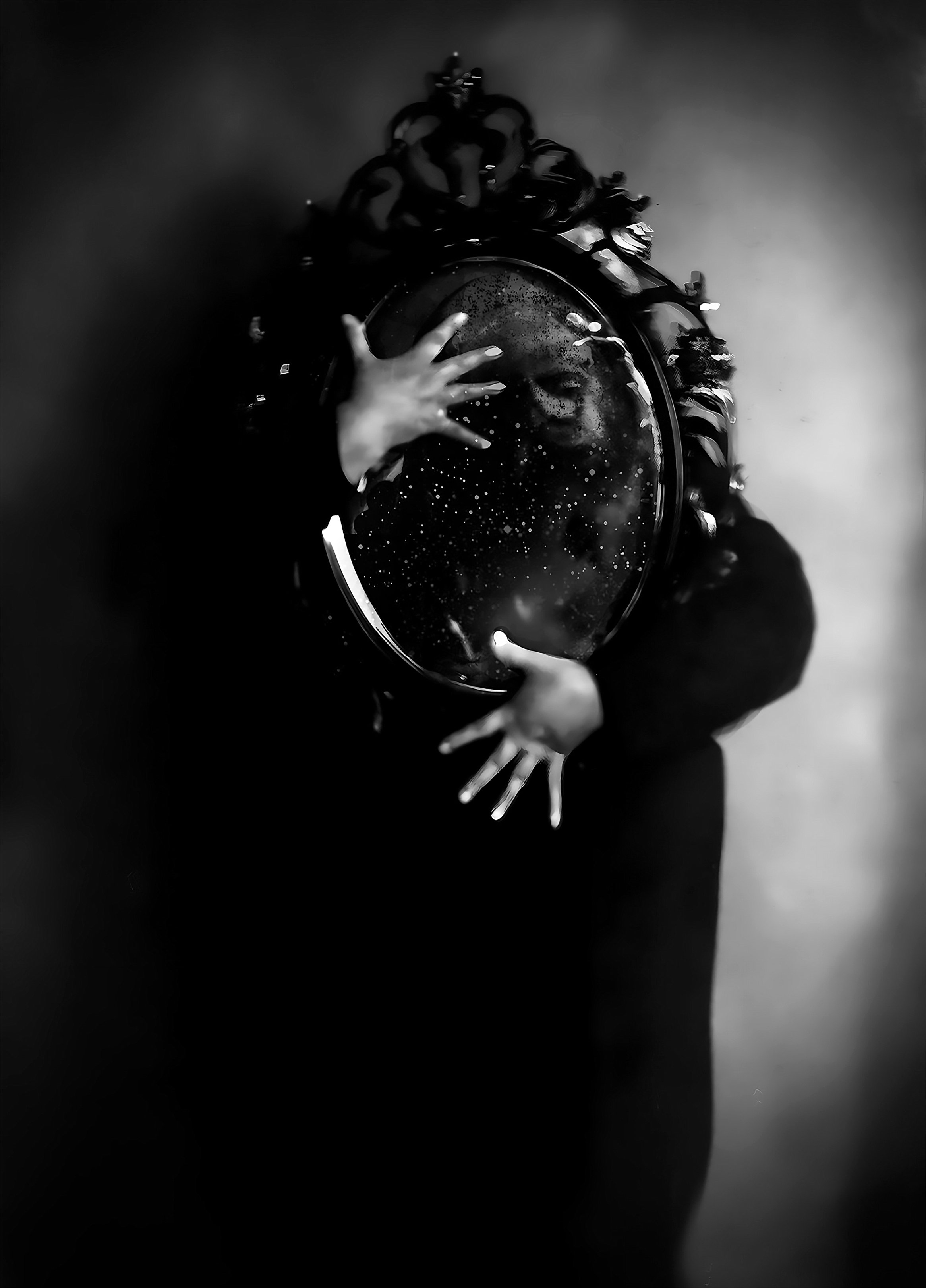 Black and white image of a person holding an ornate oval mirror, with hands on the surface.