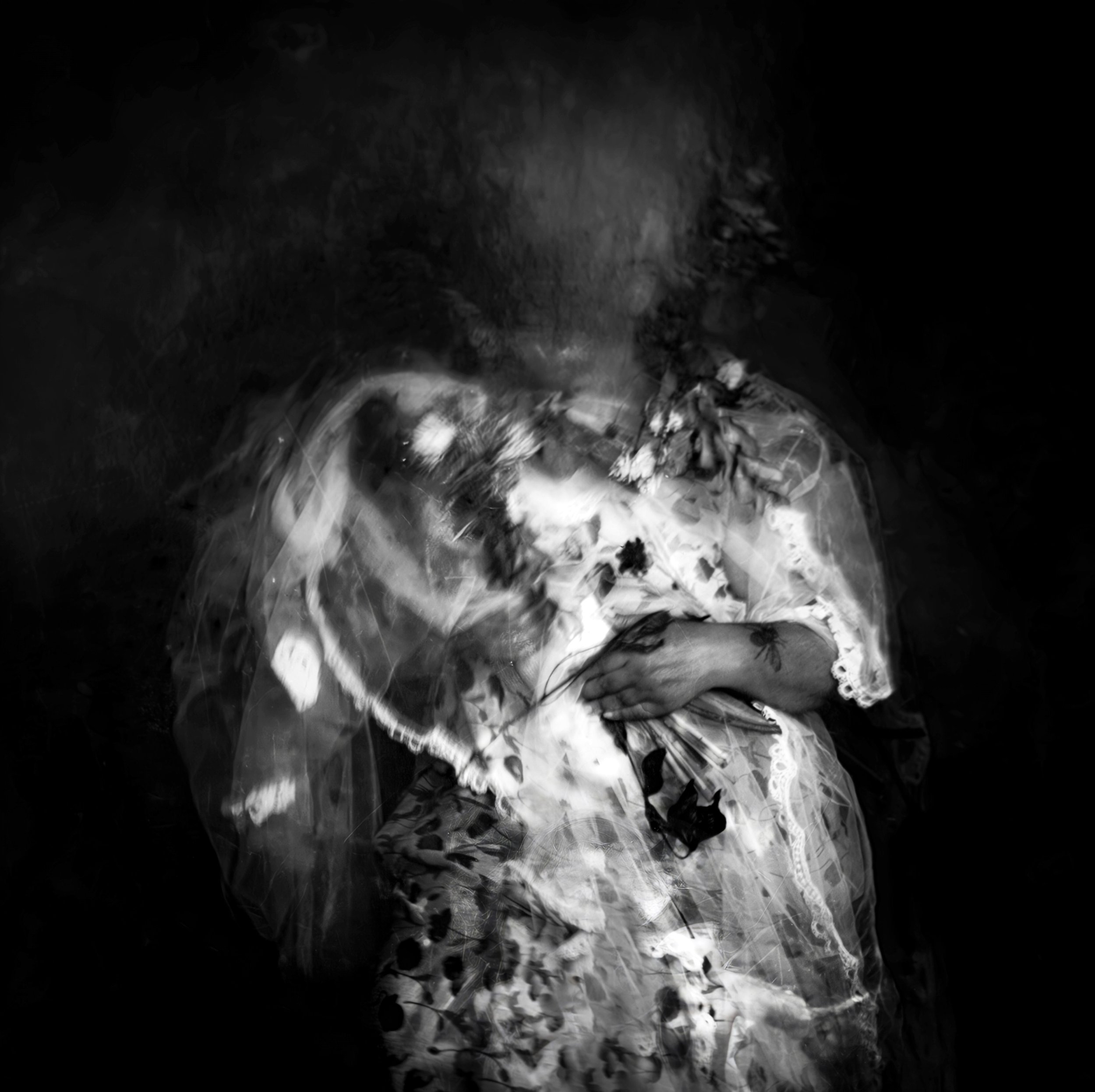 Abstract black and white image of a person with blurred, ghostly appearance, holding flowers and dressed in a floral patterned fabric.