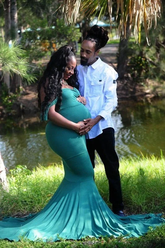 Pregnant woman in green dress with partner by a pond in nature.