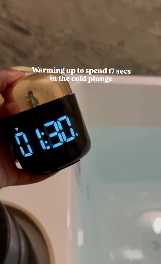 A hand holding a small device with a digital display showing 1:30, near a bathtub filled with water, with a caption warning about cold plunge.