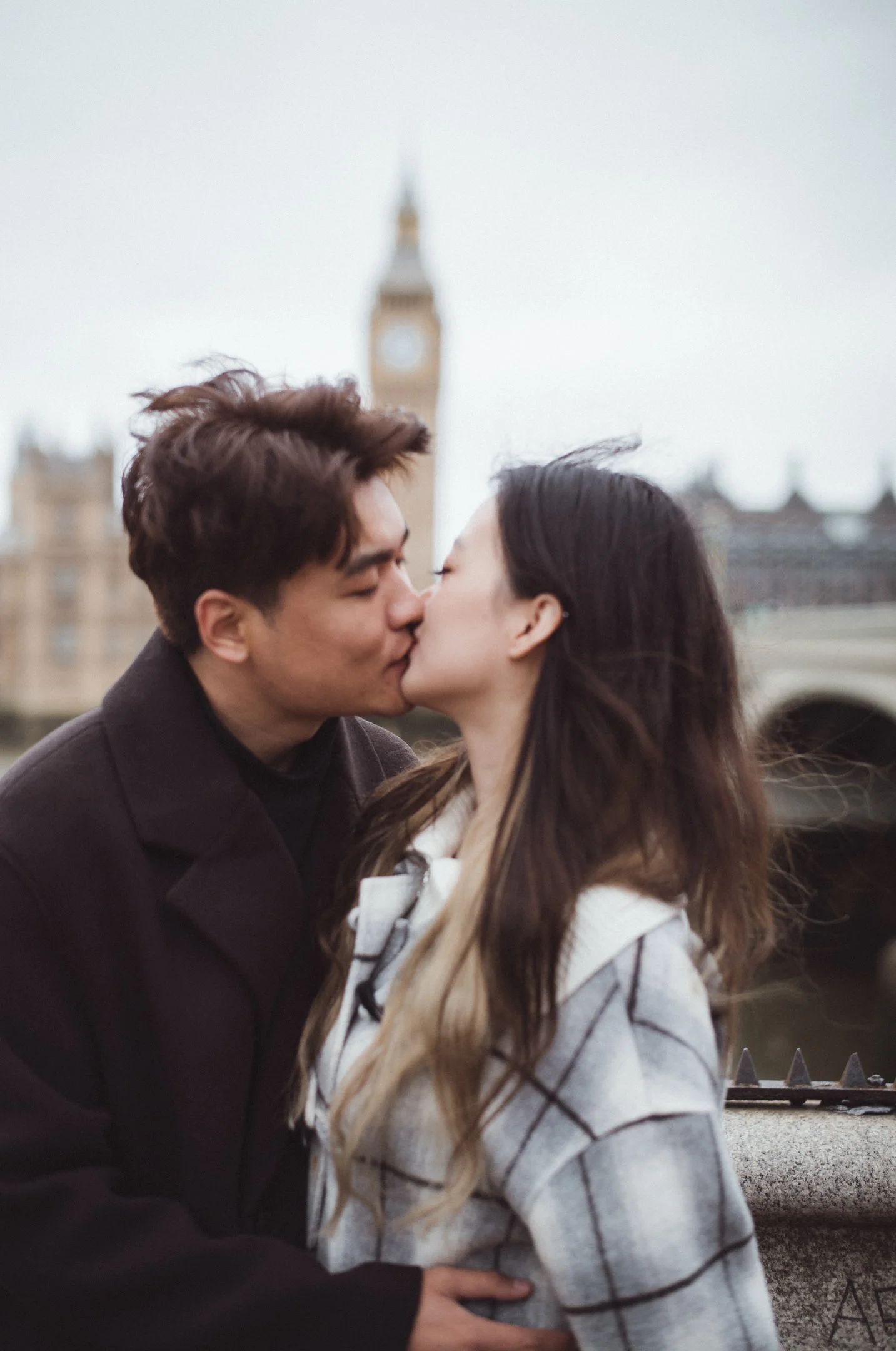 A young man and woman kissing outdoors with Big Ben in the background.