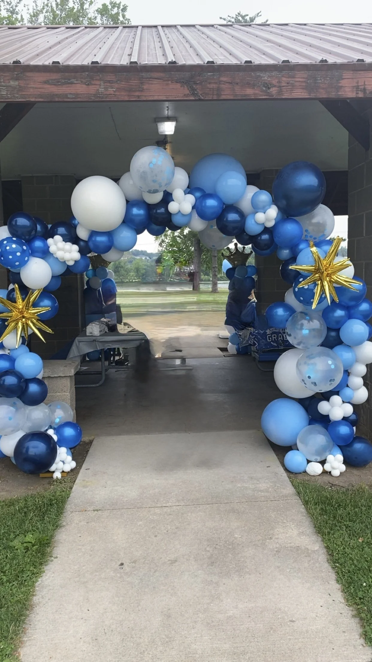 A woman with natural curly hair wearing a colorful patterned sleeveless dress stands with hands on hips against a light green background.