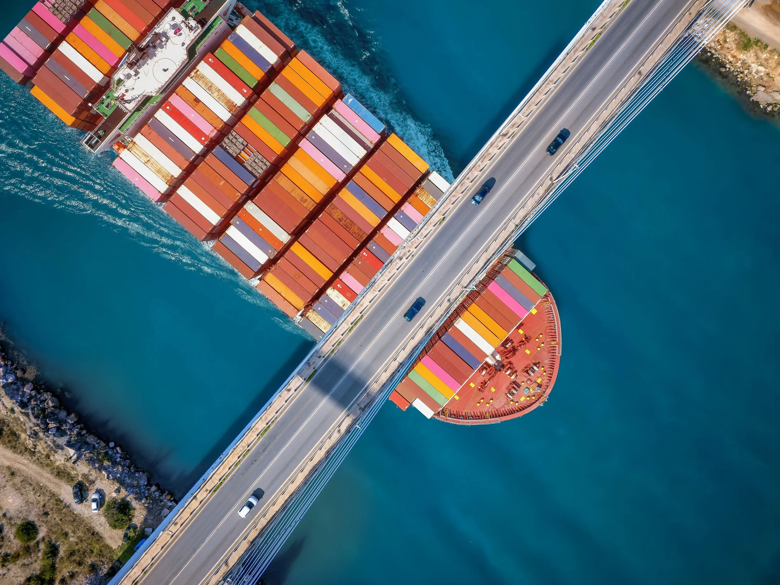 Container ship passing under a bridge in a narrow channel, symbolizing how trade corridors and chokepoints shape global economic power.