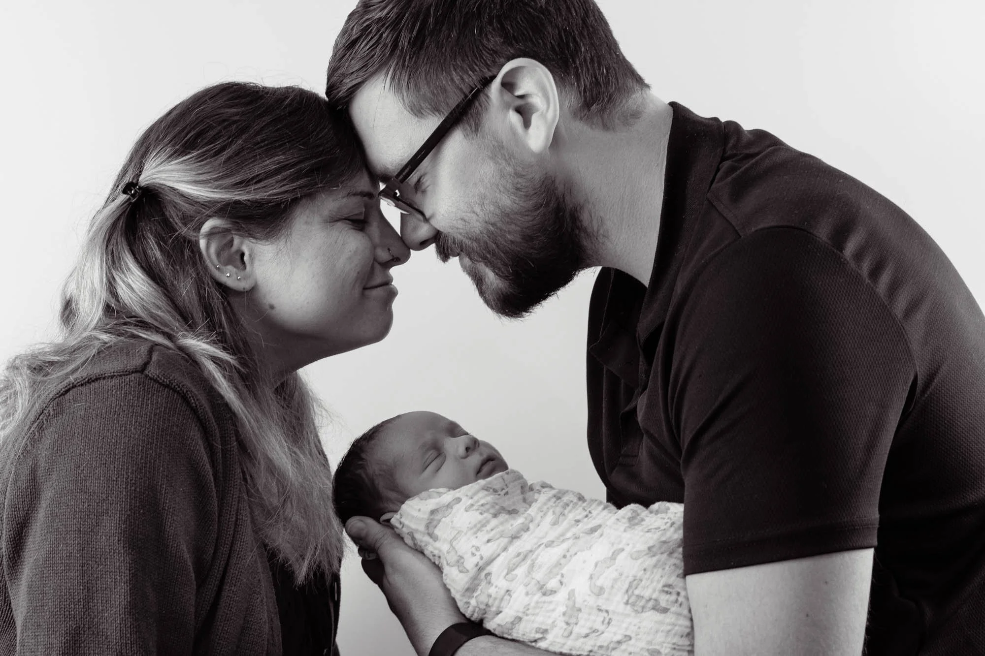 A couple holding their newborn baby, their foreheads touching, in a tender and intimate moment.