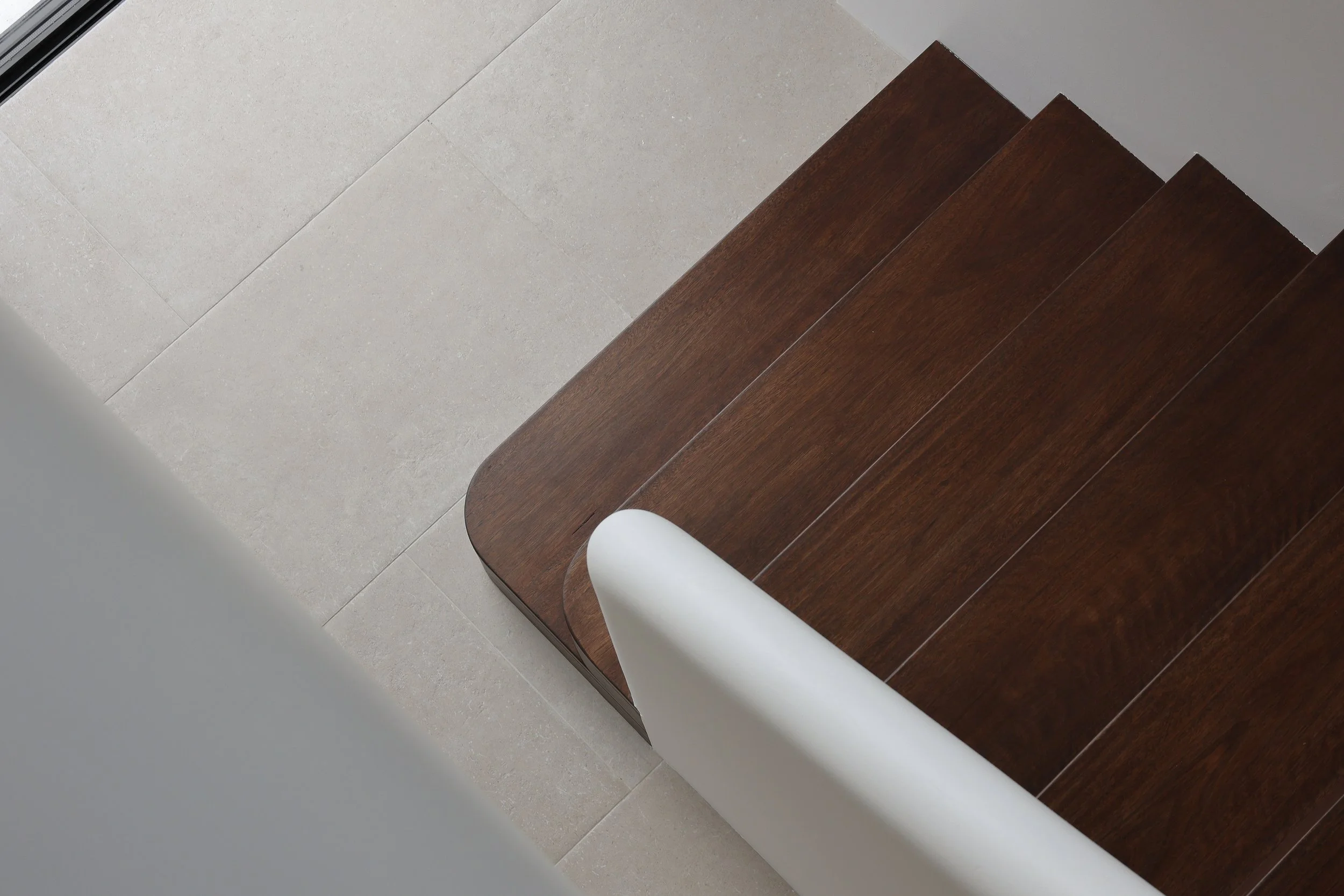 Close-up of a modern interiors with light-colored tile flooring, a curved wooden bench, and a white cylindrical object.