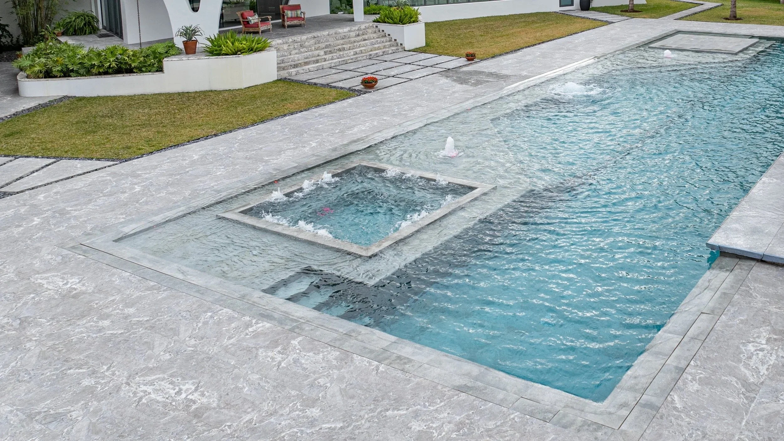 A side perspective along the pool's length, highlighting the custom square spa with deck jet bubbler set seamlessly into the pool deck — expert craftsmanship in every detail from coping to water features.
