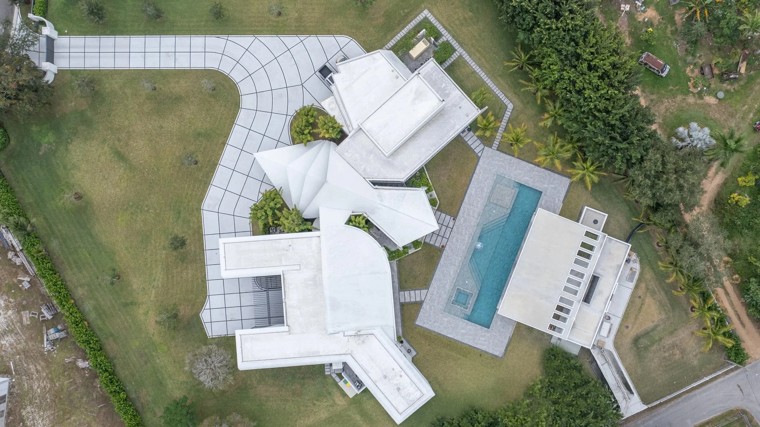 Drone overview of the full estate highlighting the unique multi-wing home design, long driveway, and the pool positioned to complement the property's layout — a project that exemplifies large-scale residential pool construction.