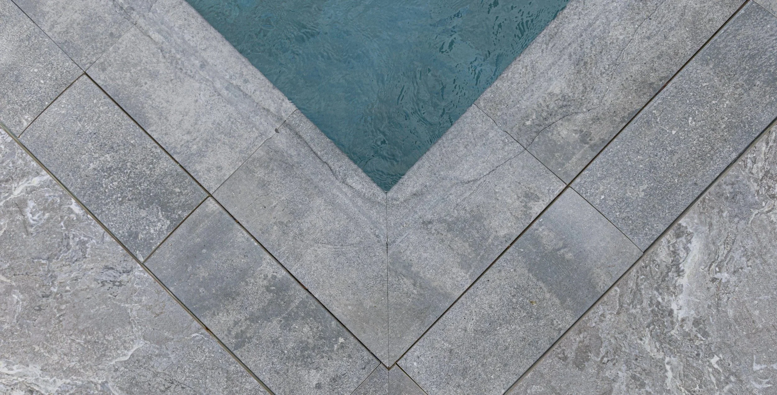 A top-down detail of the pool corner showing the precisely cut geometric stone coping pattern — a testament to the premium materials and expert tilework that define our finished pools.
