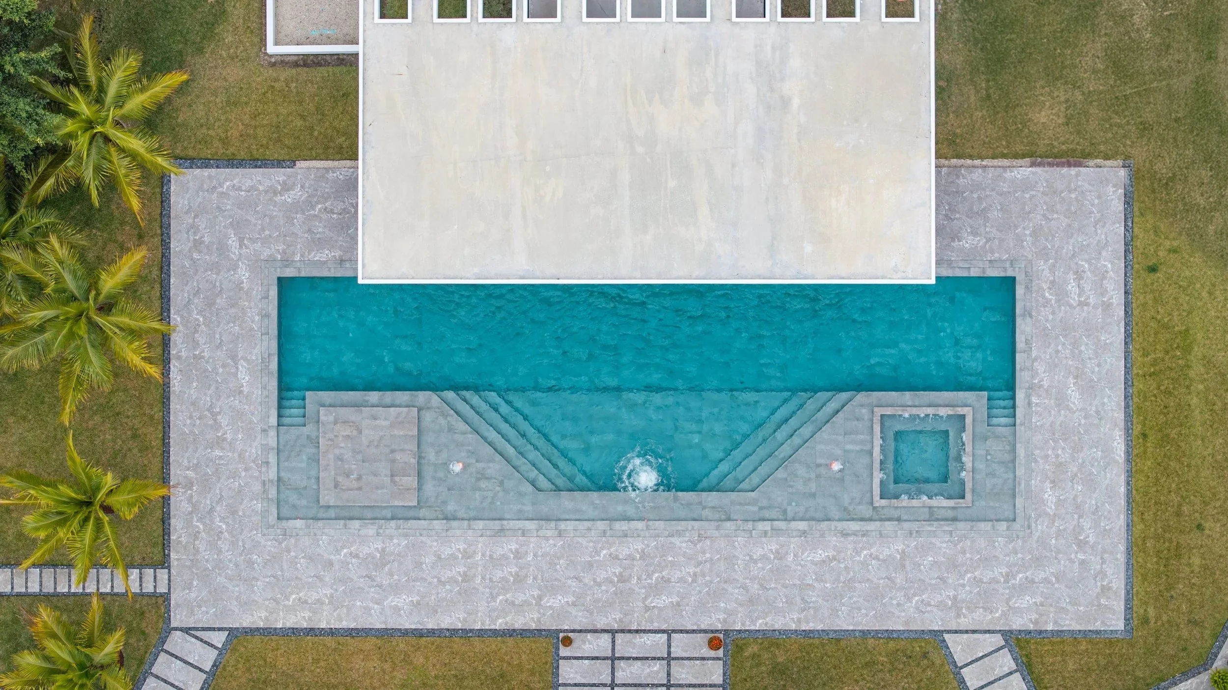 Aerial view of a stunning rectangular pool design featuring a clean geometric layout, custom stone paver deck, and integrated spa — showcasing the precision and craftsmanship of our residential pool construction.