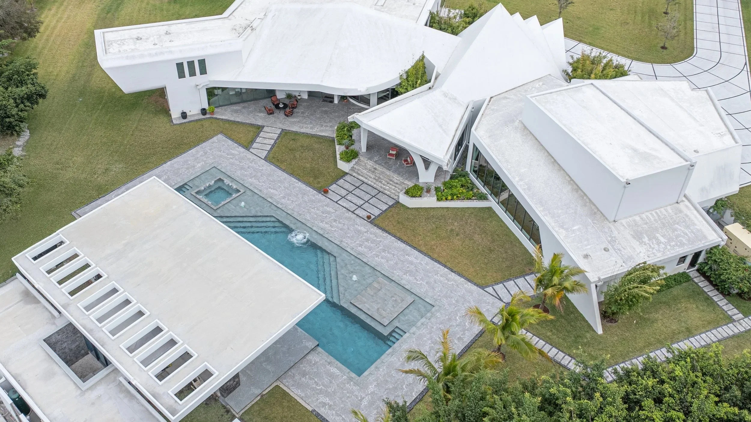 Aerial perspective of the full property showing the pool and spa in context with the home's distinctive multi-gabled roofline — a one-of-a-kind residential pool project seamlessly integrated into a stunning estate.