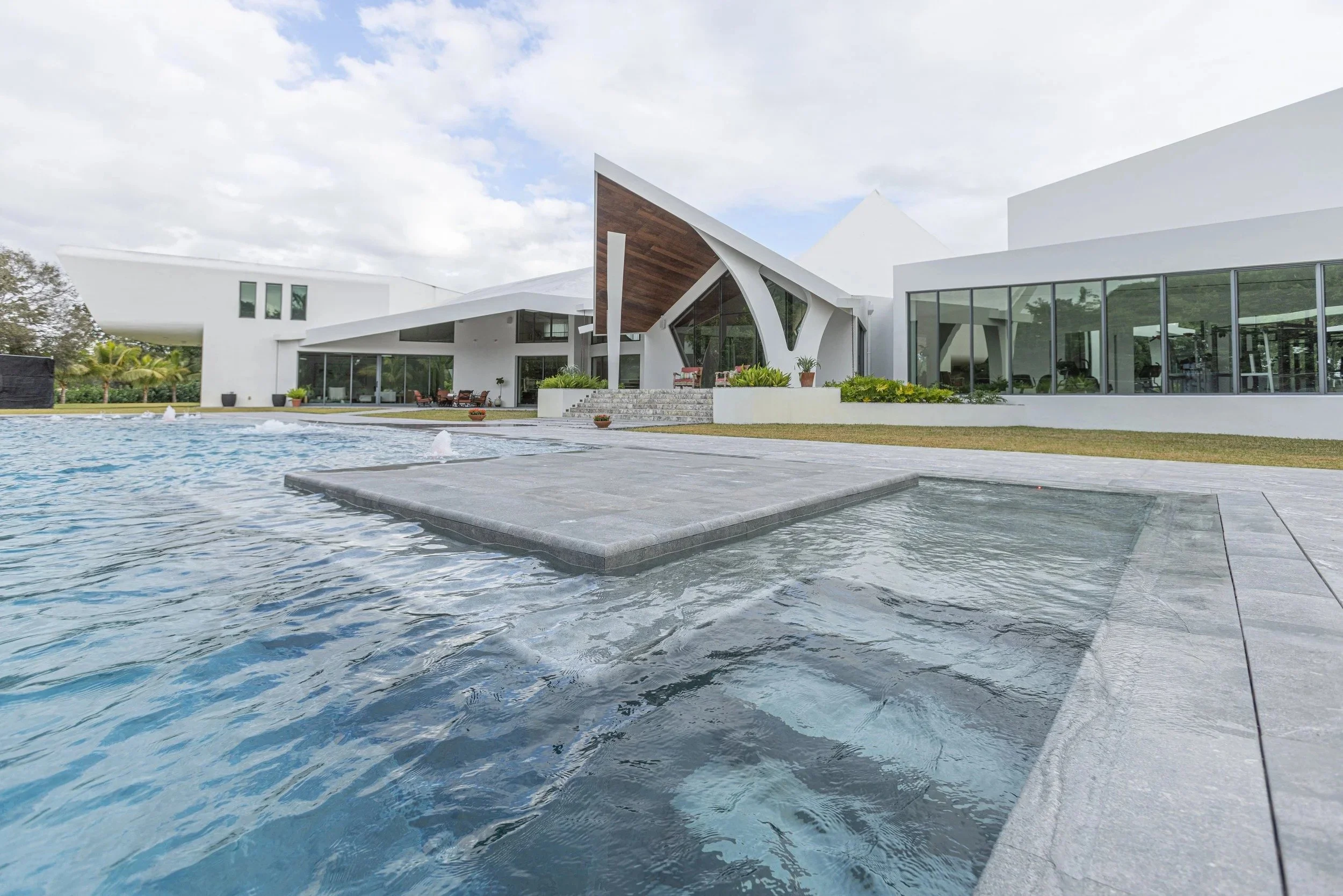 A water-level perspective featuring a submerged tanning ledge with the home's iconic triangular roofline reflected in the still pool water — the ideal balance of relaxation and architectural beauty.
