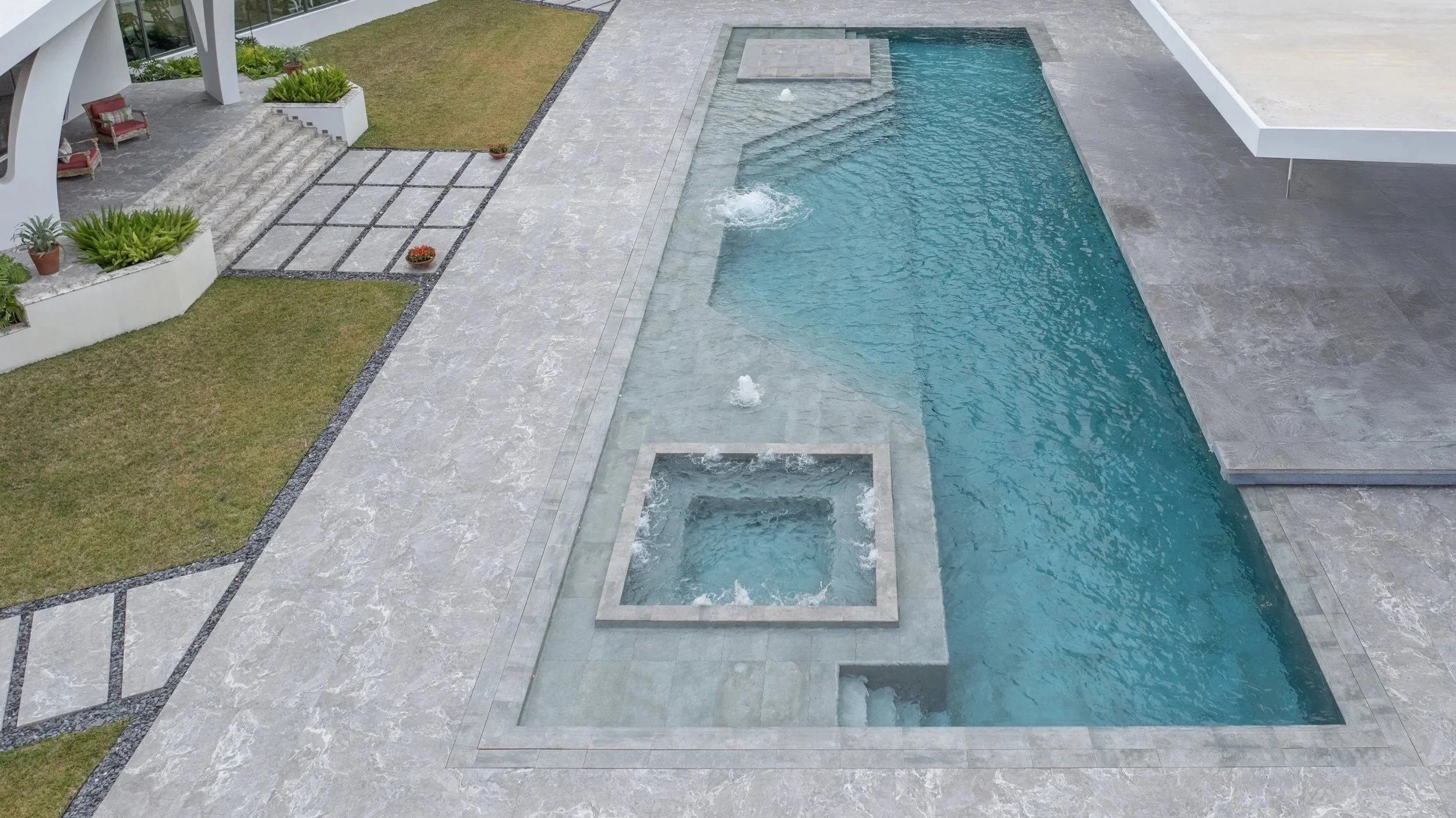 An overhead view of the full-length lap pool with integrated square spa, wide stone deck surround, and custom entry steps — a beautifully cohesive design that combines function and luxury.