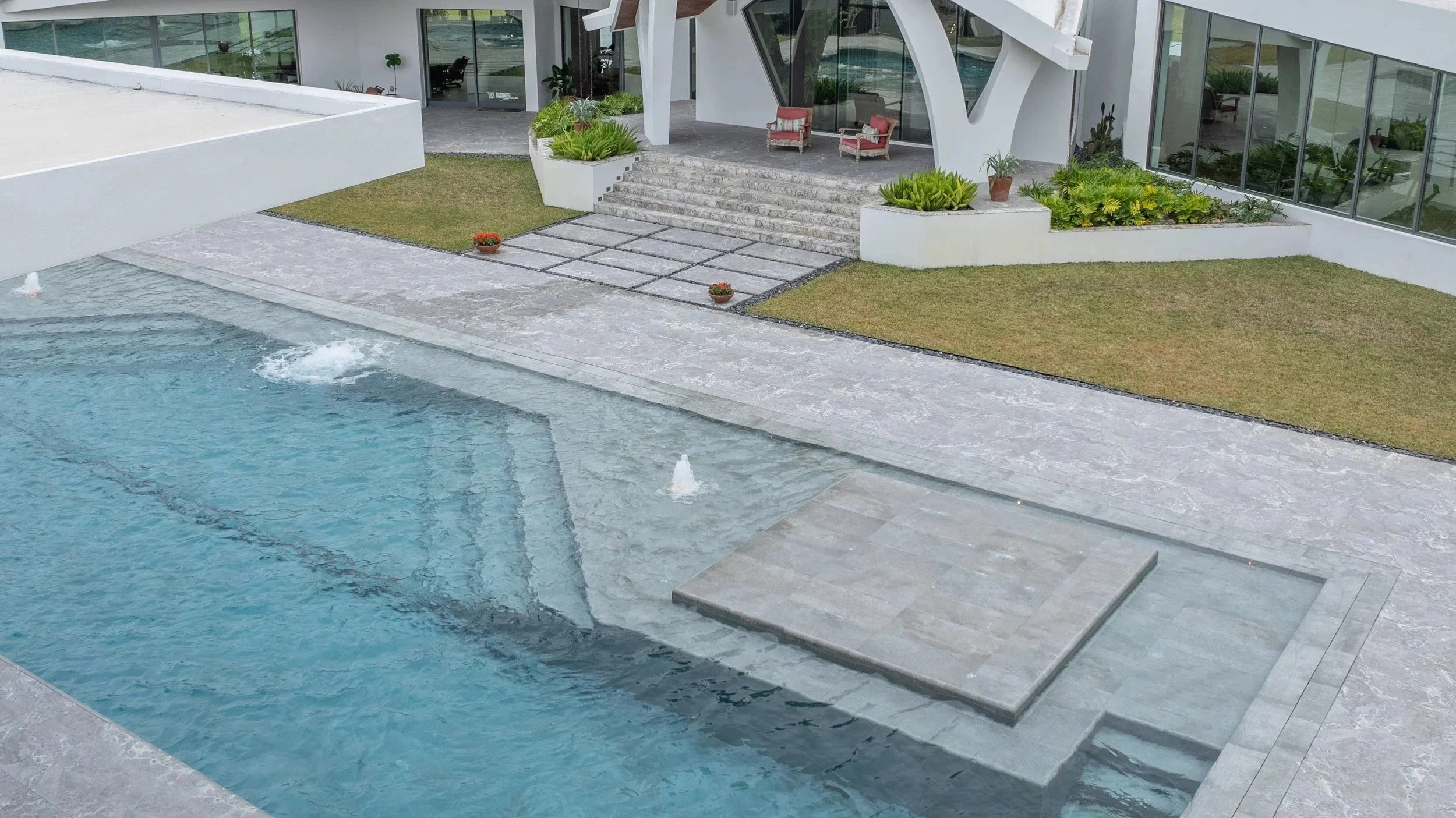 An angled view of a cusAn angled overhead shot capturing the full pool area nestled between two wings of the luxury estate, complete with tanning ledge, integrated spa, and lush tropical surroundings.tom pool featuring a tanning ledge, integrated ent