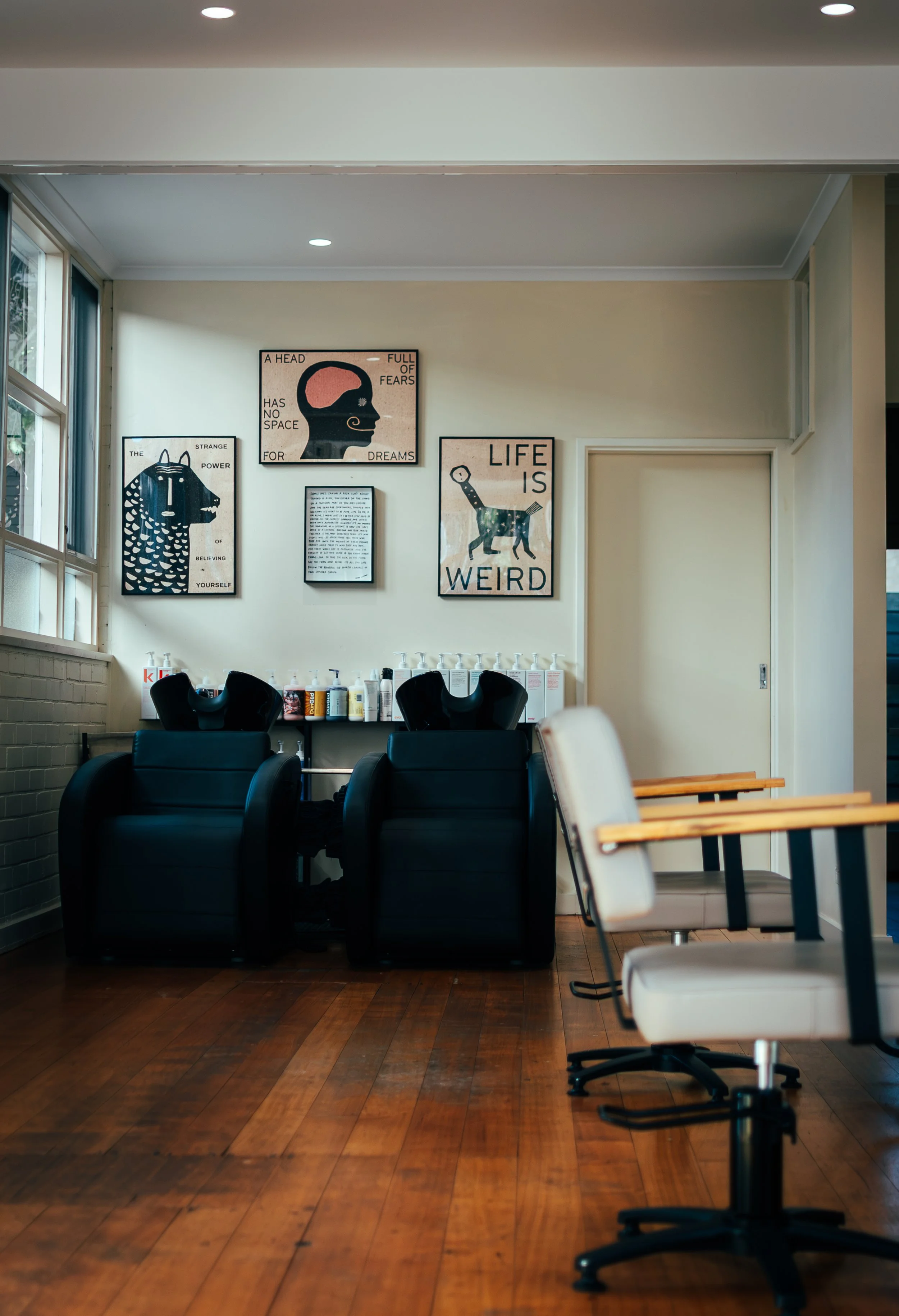 Interior of a hair salonwith black shampoo chairs, white styling chairs, and wall art featuring illustrations and quotes about life and dreams.