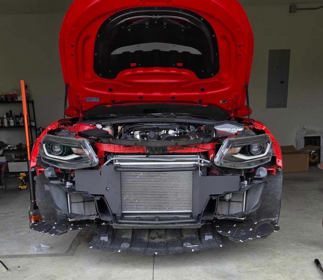 A red Camaro ZL1 being worked on in a garage.
