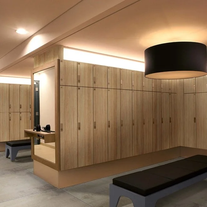 Locker room with wooden lockers, bench seating, and a black hanging ceiling light, in a modern design.