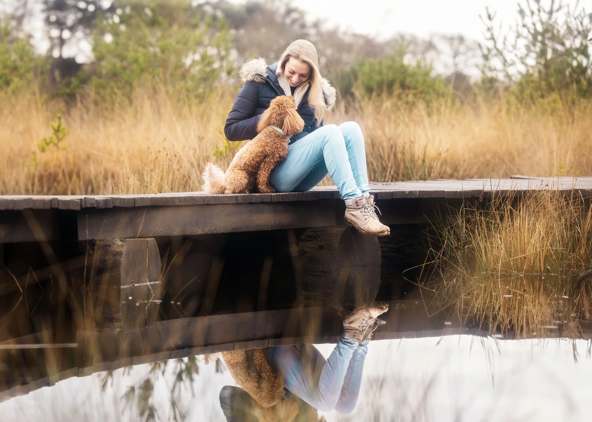 Eine Frau genießt auf einem Steg sitzend einen Moment mit ihrer kleinen Hündin während eines Outdoor Fotoshootings für Menschen und ihre Hunde. Januar 2026.