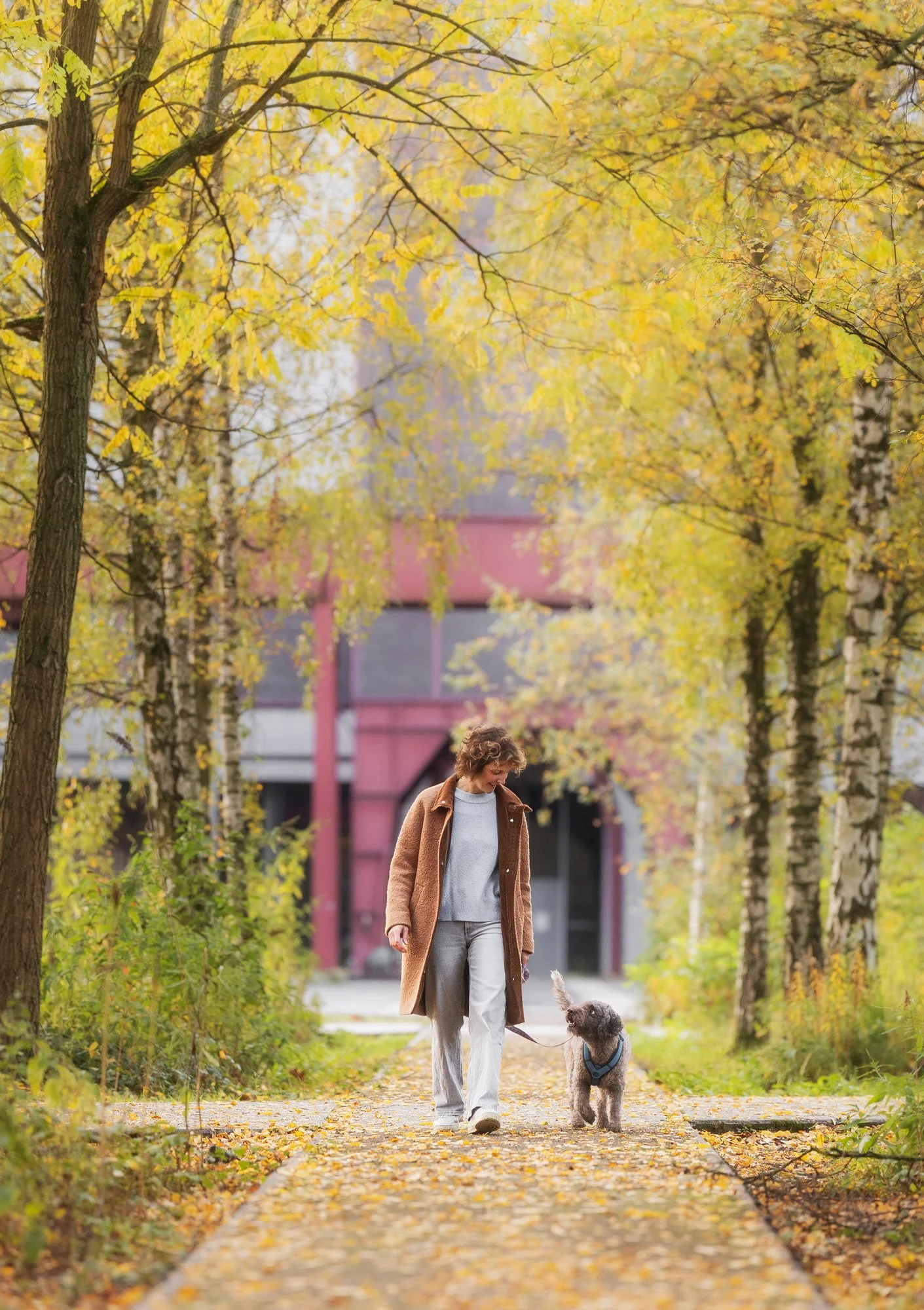 Eine Frau läuft während eines Outdoor Fotoshootings mit ihrem Hund durch eine herbstliche, alte Industriekulisse und beide sehen sich gegenseitig an. März 2026.