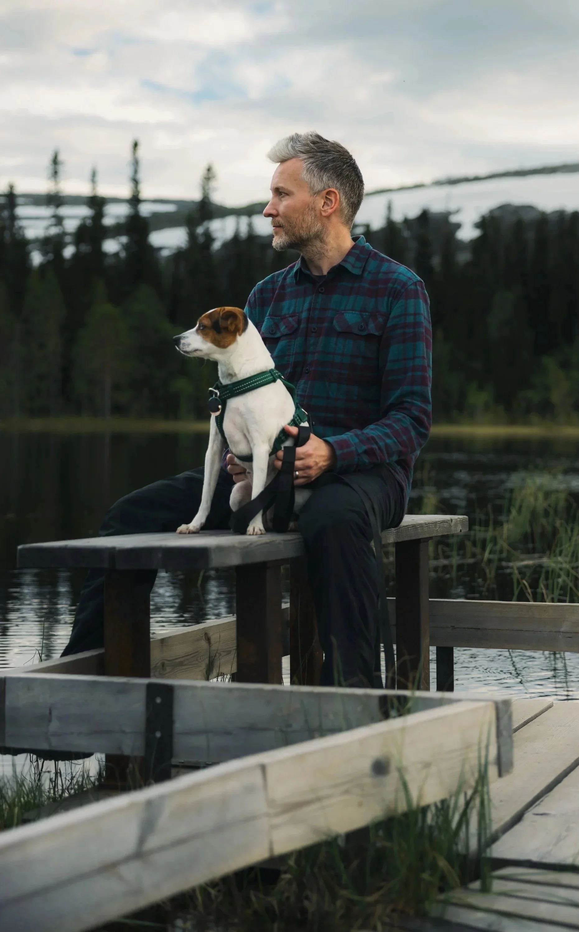 Ein Bild vom Autor der Website, der mit seinem Hund auf einer Bank sitzt. Im Hintergrund sind Berge, Bäume und ein See zu sehen.