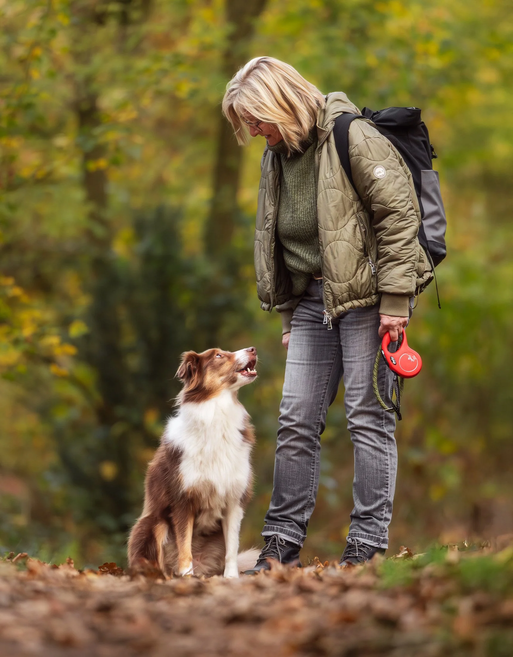 Eine Hundebesitzerin wechselt einen lustigen Blick mit ihrem Hund während eines Fotoshootings im herbstlichen Wald