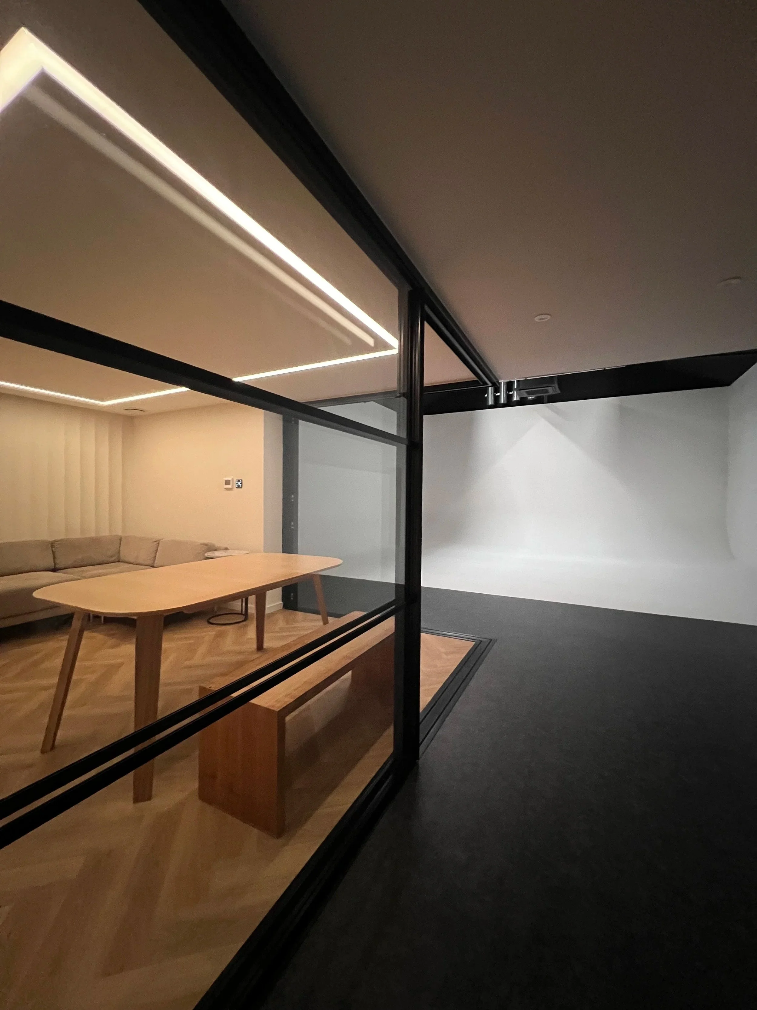 view from entrance to Studio B at Shutters Studios in Acton, West London. We see the tv lounge/podcasting room on the left, half open glazed partition door and further down there is the stunning cyclorama with blackout blinds opened just a crack