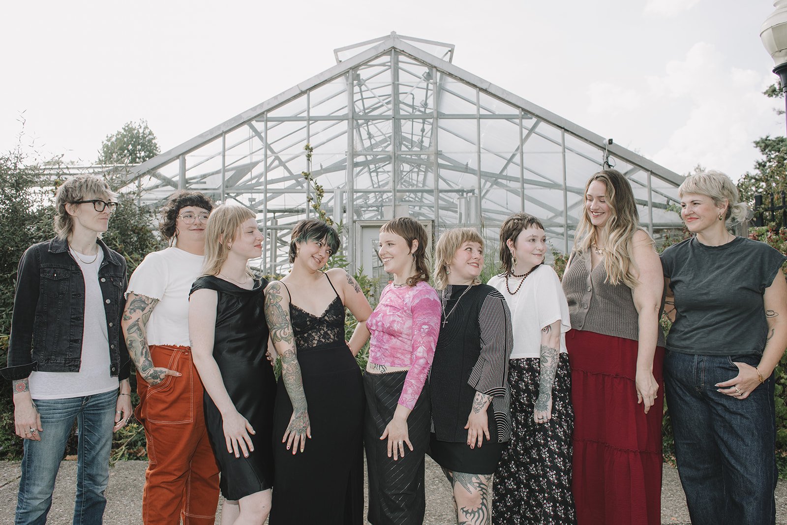 Group of women standing outside in front of a glass greenhouse, smiling and looking at each other.