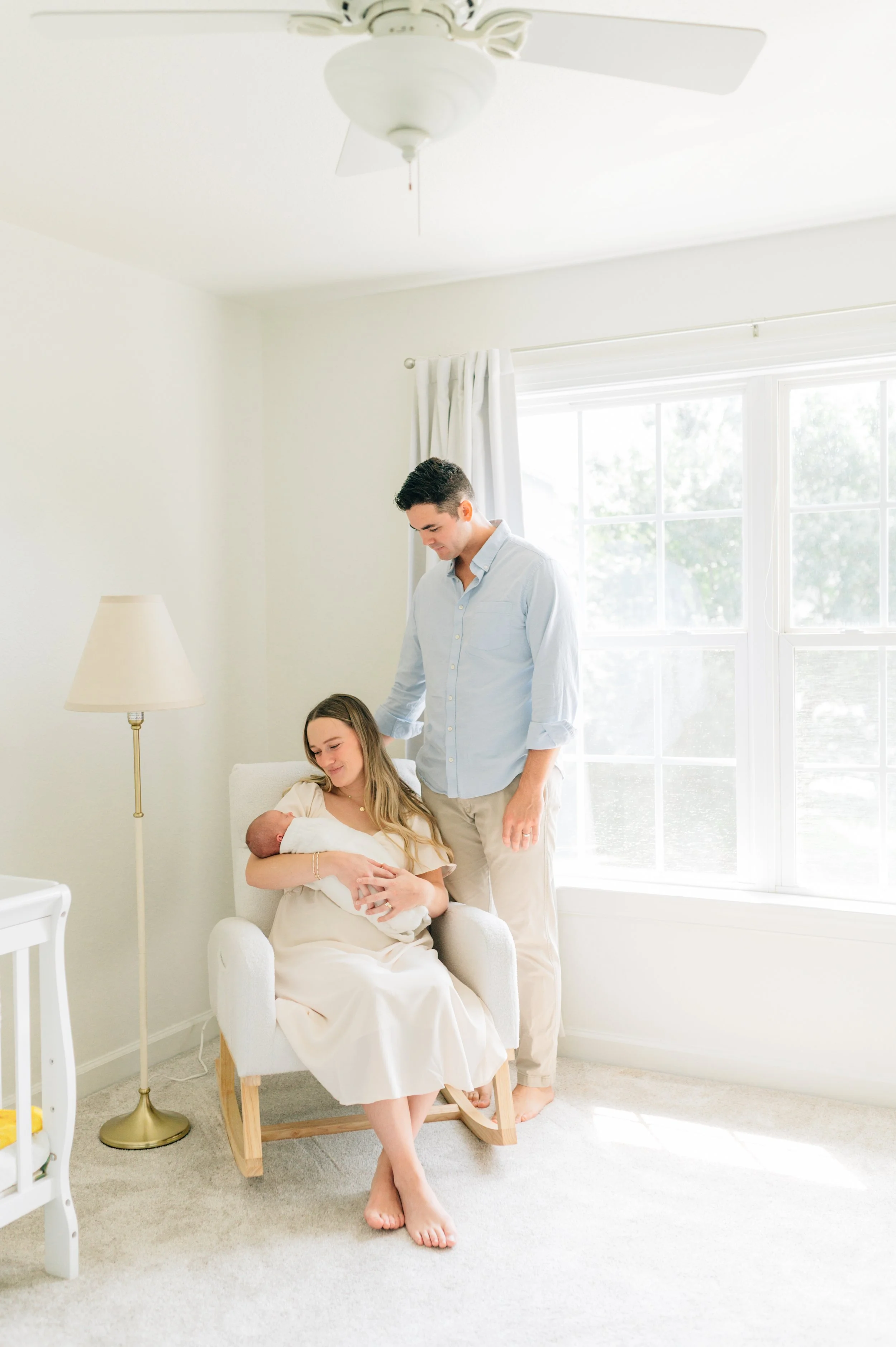 Family lying on bed with baby, two adults and a toddler, indoor plants in background