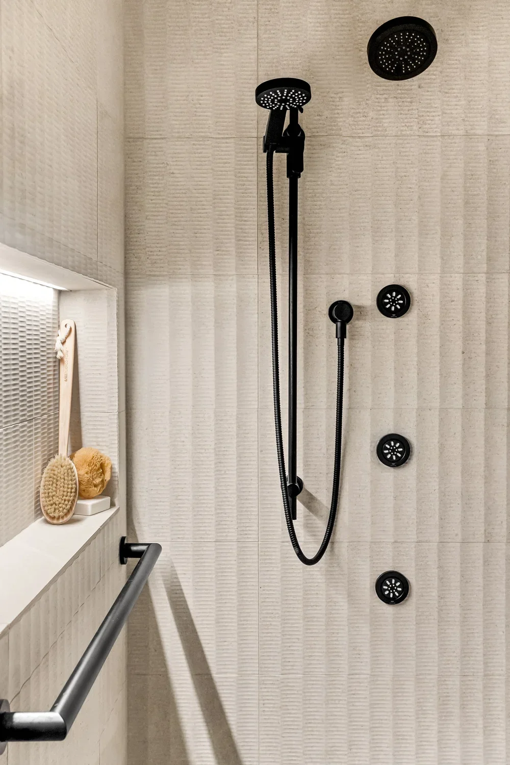 Shower with black rainfall showerhead, handheld showerhead, and three body jets on a beige tiled wall.