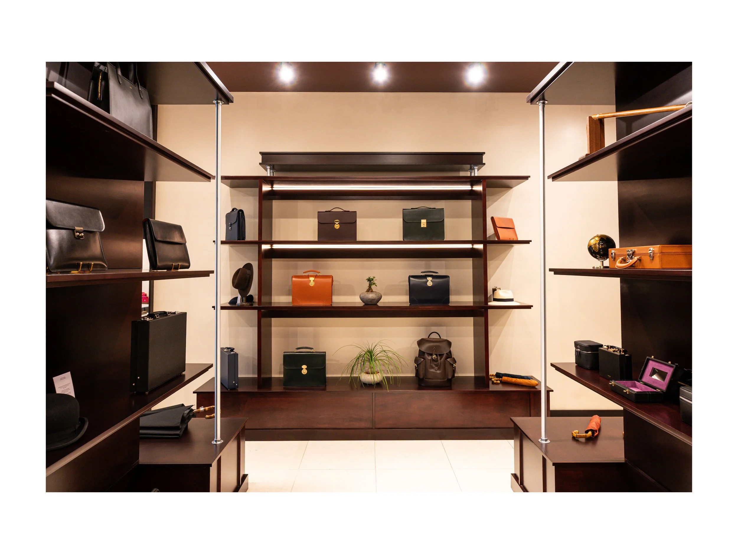 Intérieur de boutique de luxe pièce en cuir à Beverly Hills, Los Angeles, états unis, avec présentoirs en bois foncé et métal, parapluies cuir et bois exotique luxe et accessoires en cuir, éclairage encastré chaleureux lumière douce et chaude