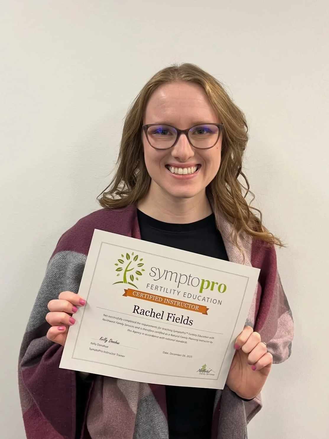 Rachel Fields, a woman with glasses and curly red hair smiling and holding a certificate from Symtpopro Fertility Education.