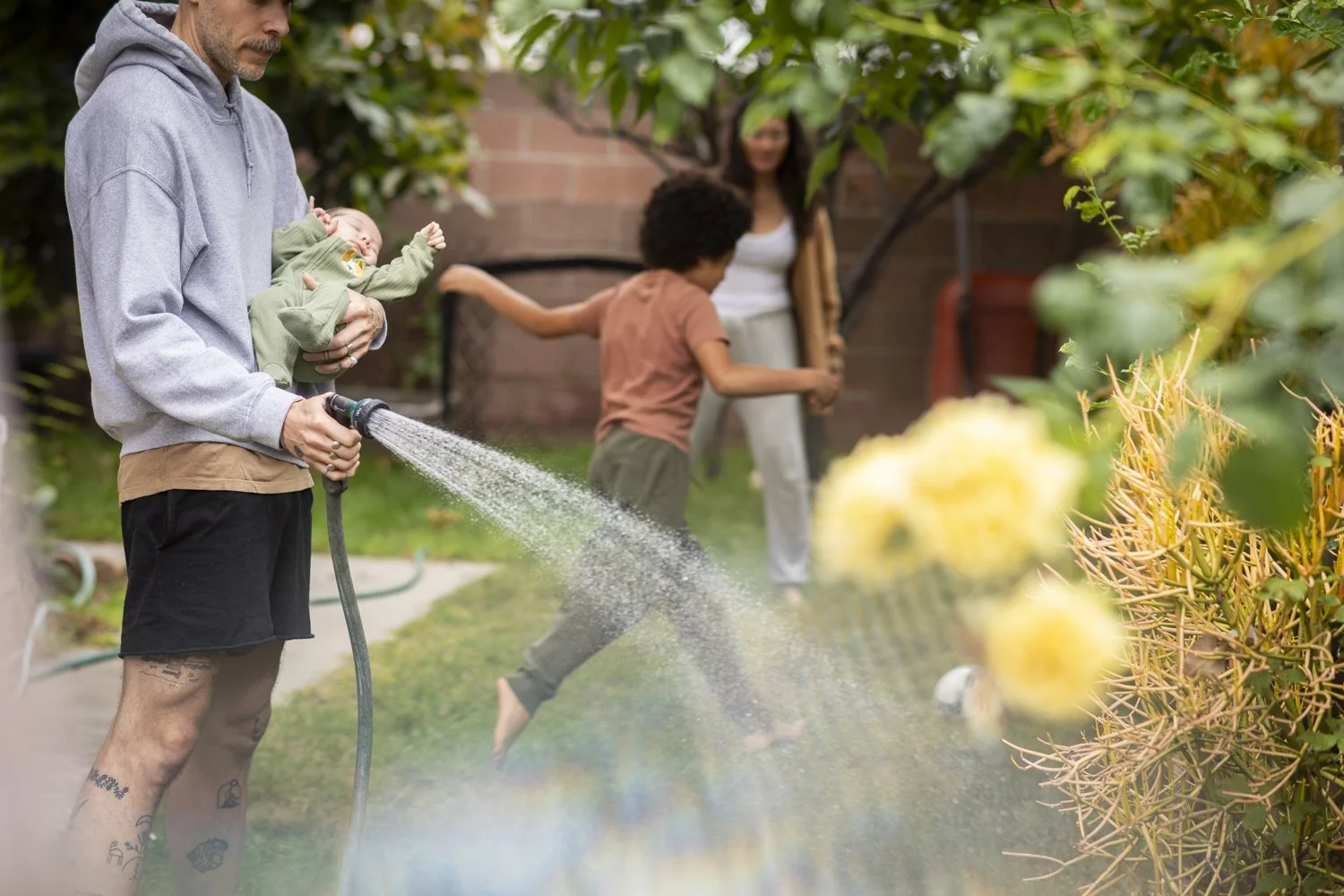 A family plays together in the garden while watering plants on a sunny afternoon.