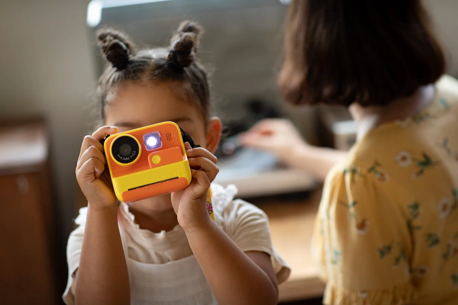 A child holds a colorful camera while photographing a family member at home.