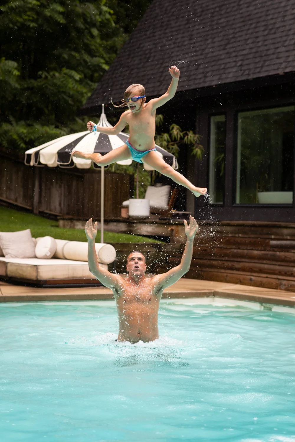 A child jumps into a swimming pool as a father reaches up from the water.