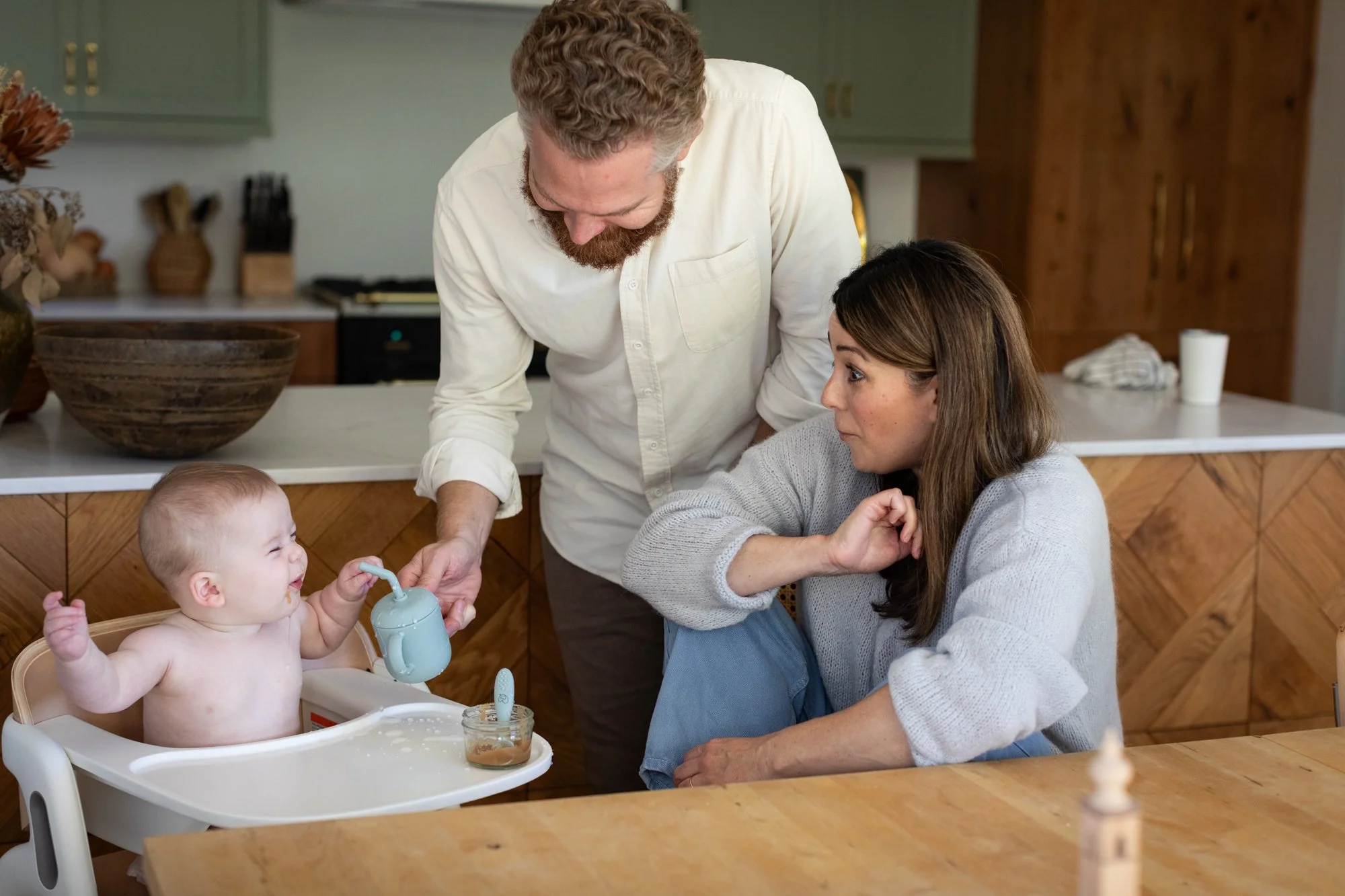 A family gathers around the kitchen table during a playful mealtime with their baby.