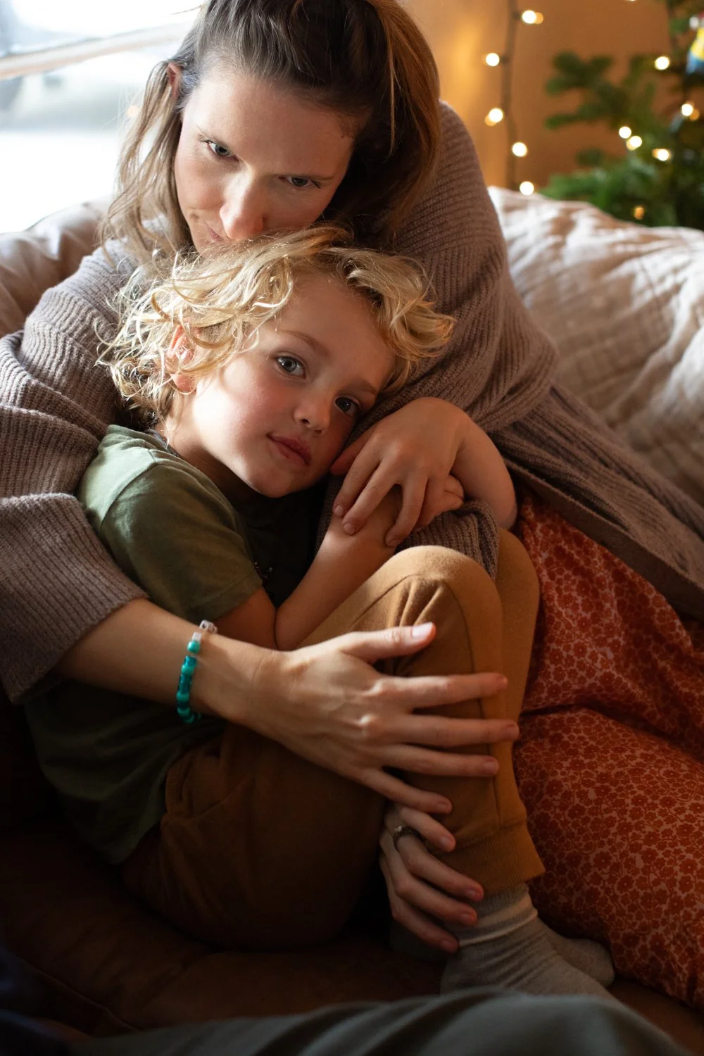 A mother and child cuddle together on a sofa, capturing a quiet moment of connection at home.