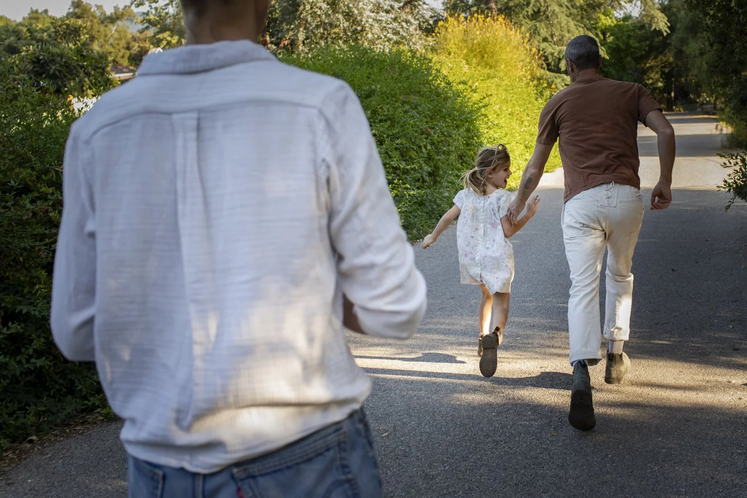 A father and daughter run down a path while another parent follows behind them.